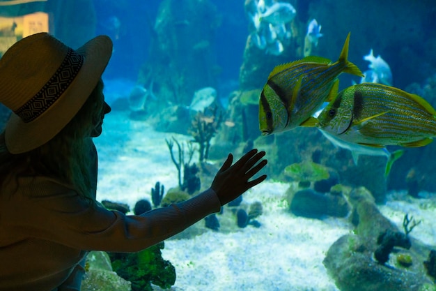 Молодая женщина прикасается к рыбе в туннеле океанариума