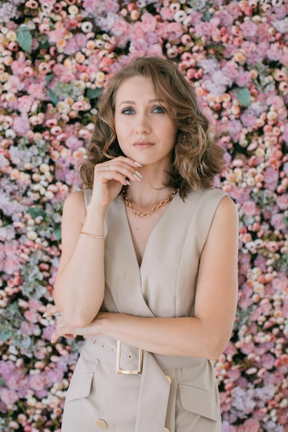 A young woman touching her chin with her fingers against the background of a wall with flowers