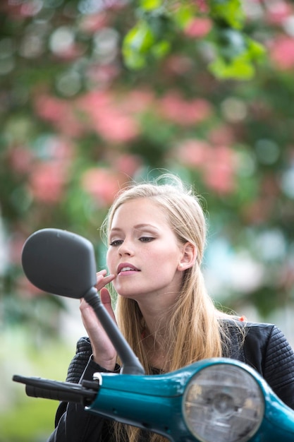 Photo young woman touching lips looking in side-view mirror of motor scooter