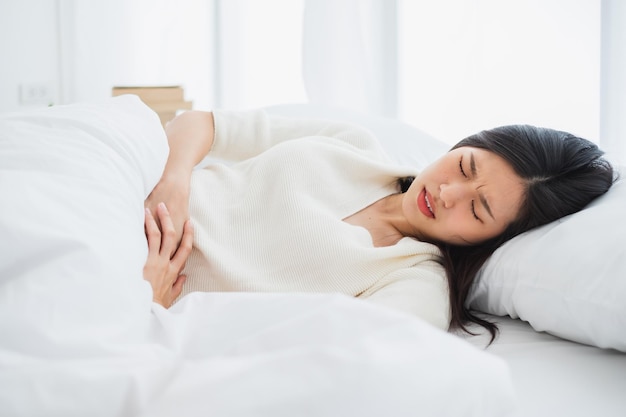 young woman touching stomach in pain while sleeping on bed