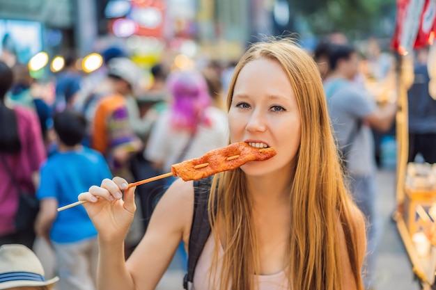 Photo young woman tourist eating typical korean street food on a walking street of seoul spicy fast food simply found at local korean martket soul korea