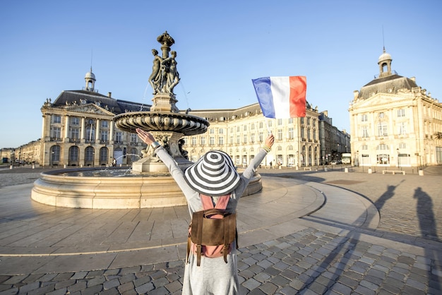 프랑스 보르도(Bordeaux) 시에서 프랑스 국기와 함께 서 있는 유명한 부르스 광장(Bourse Square)에서 아침 전망을 즐기는 젊은 여성 관광객