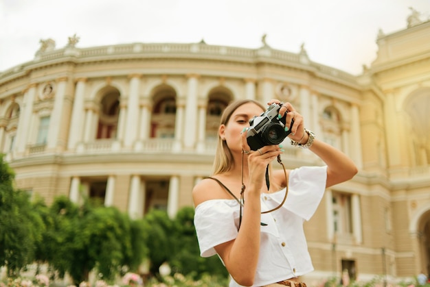 若い女性の観光客は彼女の手でレトロなカメラを保持します