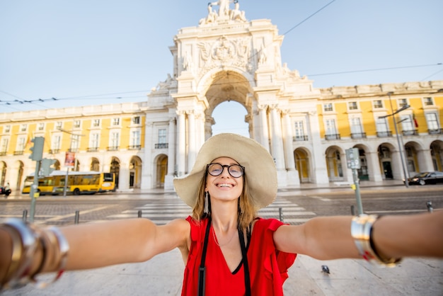 Фото Молодая женщина-турист делает селфи перед знаменитой триумфальной аркой, путешествуя по городу лиссабон в португалии