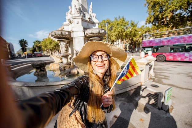 バルセロナ市の噴水の近くにカタロニア語の旗でselfie写真を作る若い女性観光客