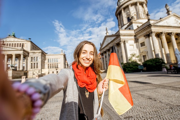 Young woman tourist making selfie photo with german flag on the French church and Opera house background in Berlin