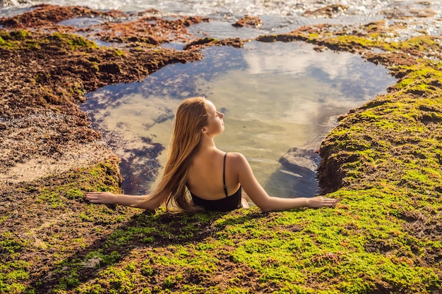 Young woman tourist on Pantai Tegal Wangi Beach sitting in a bath of sea water Bali Island Indonesia Bali Travel Concept