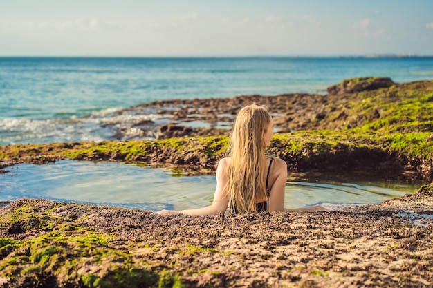 Young woman tourist on Pantai Tegal Wangi Beach sitting in a bath of sea water Bali Island Indonesia Bali Travel Concept