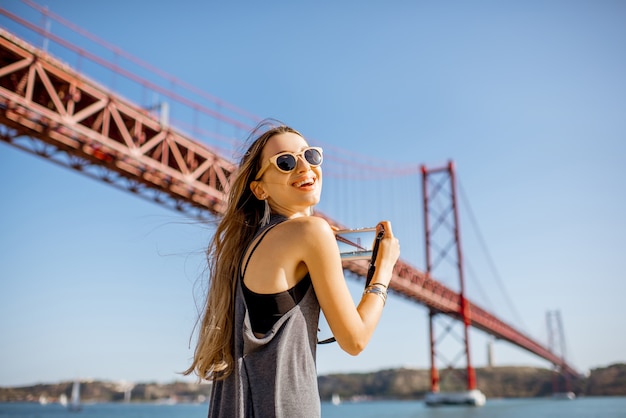 Молодая женщина турист фотографирует знаменитый железный мост в городе Лиссабон, Португалия