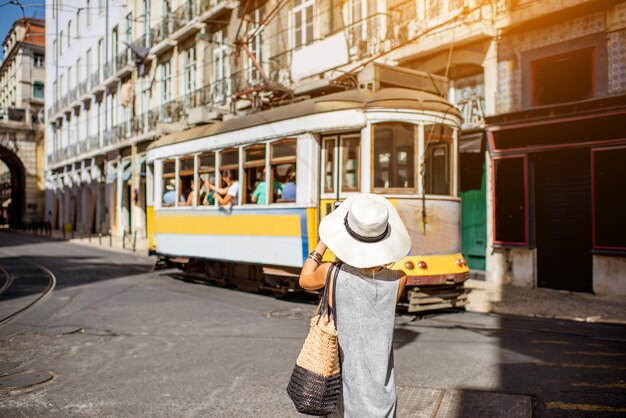 ポルトガルのリスボン市を旅する有名なレトロな黄色の路面電車を撮影する若い女性の観光客