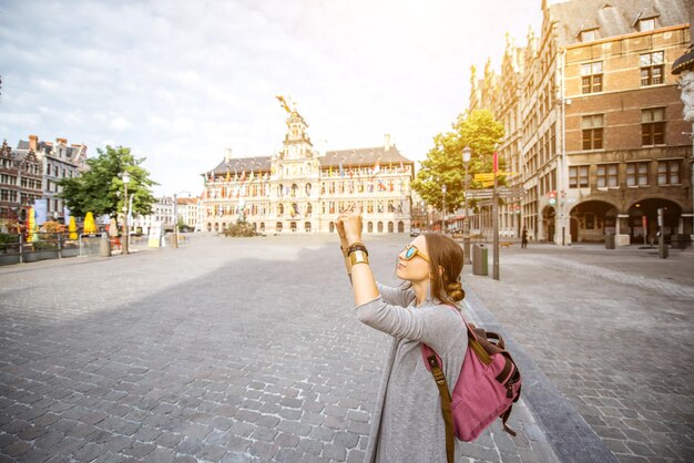 Photo young woman tourist photographing wiht phone on the great market square in antwerpen, belgium