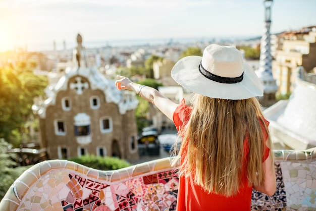 Young woman tourist in red dress enjoying great view on Barcelona city in famous Guell park