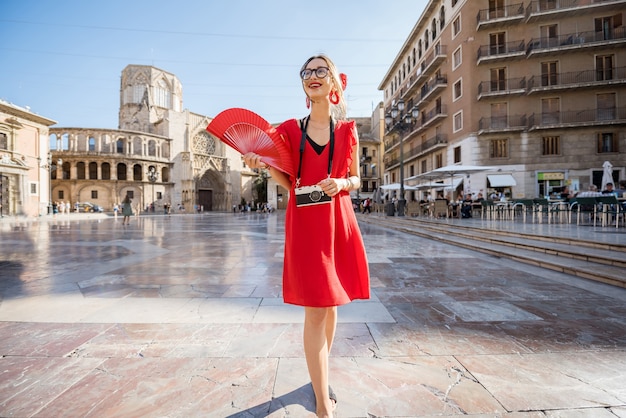 Молодая женщина-турист в красном платье с веером идет на центральной площади города Валенсия, Испания