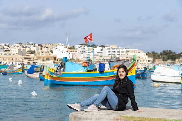 Marsaxlokk의 다채로운 보트로 가득한 바다를 배경으로 앉아 있는 젊은 여성 관광객