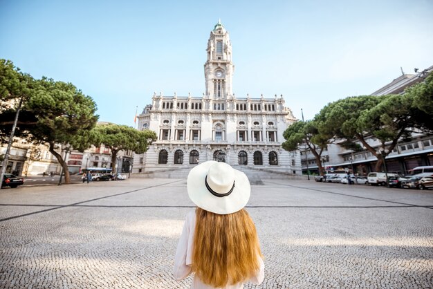 Young woman tourist in sunhat standing back in front of the city hall building during the morning light in Porto, Portugal