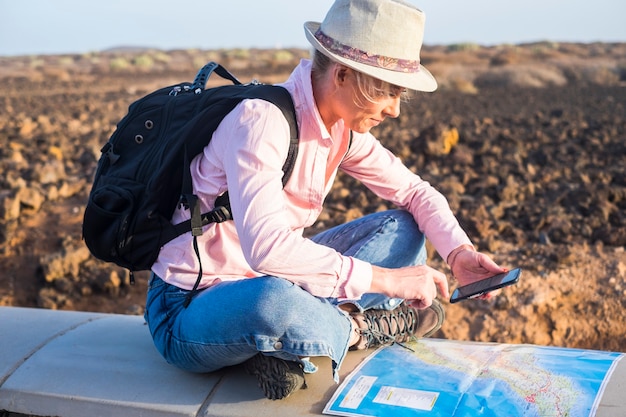 Young woman tourist travel with backpack looking for next step reading map and internet on mobile phone technology - hiker and trekker alternative lonely vacation to explore and enjoy the world - free