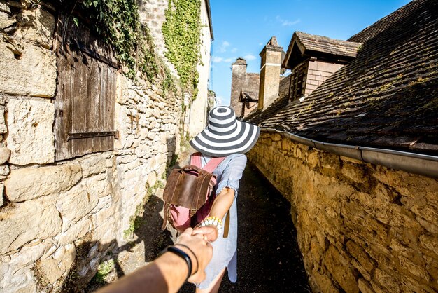 Young woman tourist with backpack and hat walking on the narrow street in the famous La Roque Gageac village in France