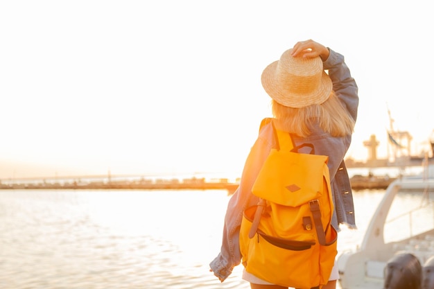 海の日の出で大きな旅行バックパックを持つ若い女性の観光客。旅行と観光のコンセプト