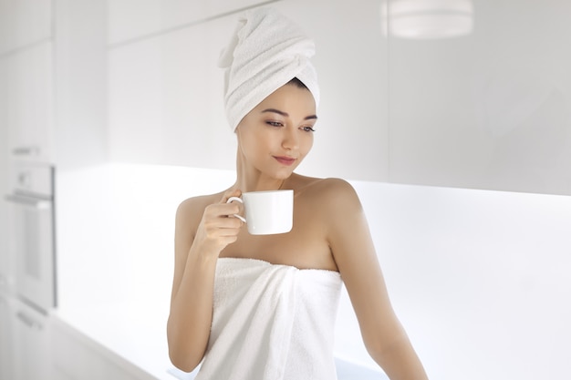 Young woman in towel enjoying coffee at home