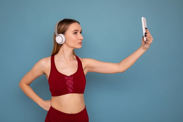 A young woman in a tracksuit and headphones takes a selfie