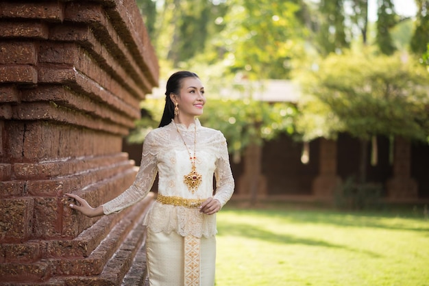 Foto giovane donna in abiti tradizionali che guarda da un'altra parte mentre si trova vicino al muro del tempio