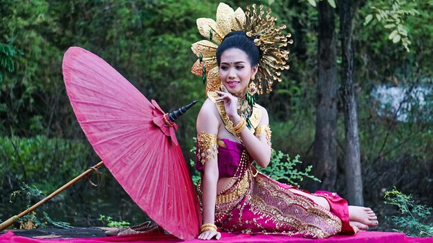 Photo young woman in traditional clothing with umbrella sitting at forest