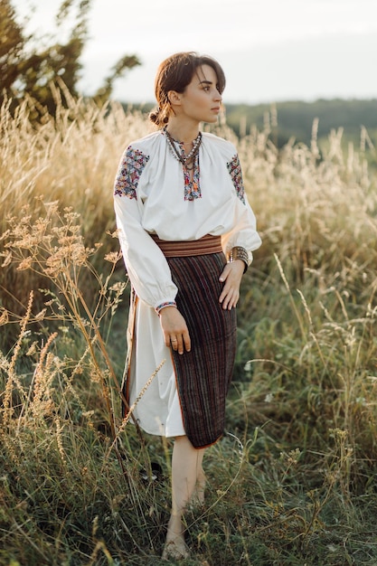 Young woman in traditional national embroidered shirt and skirt\
on nature at sunset ethnic national clothes style embroidered\
shirt