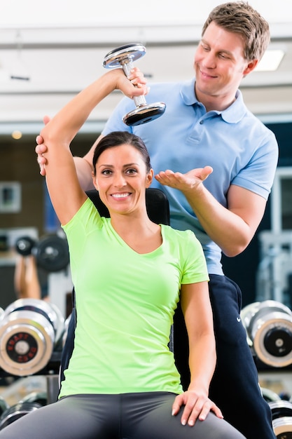 Young woman and trainer at exercise in gym with dumbbell weights