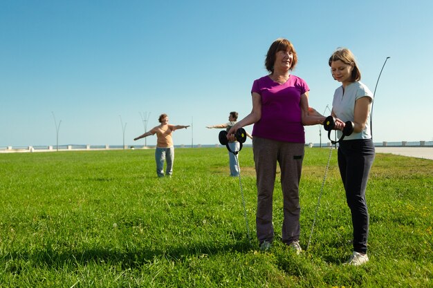 Young woman trainer helps senior woman doing stretching exercises