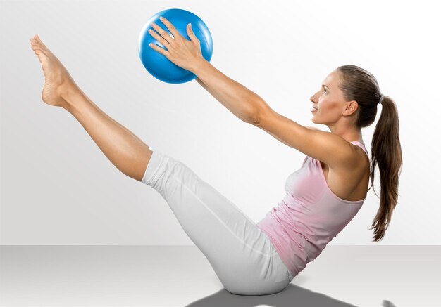 Фото Тренировка молодой женщины с фитнес-мячом на сером фоне