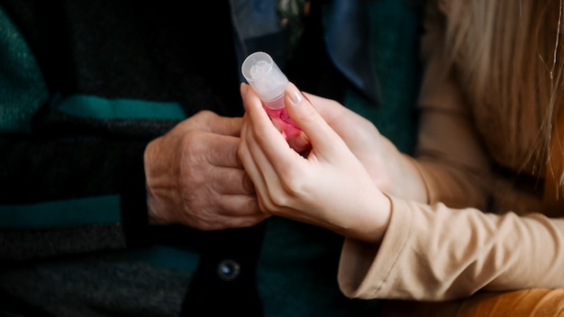 Young woman trains an elderly grandmother to treat her hands with antiseptic during the quarantine period of the coronavirus pandemic