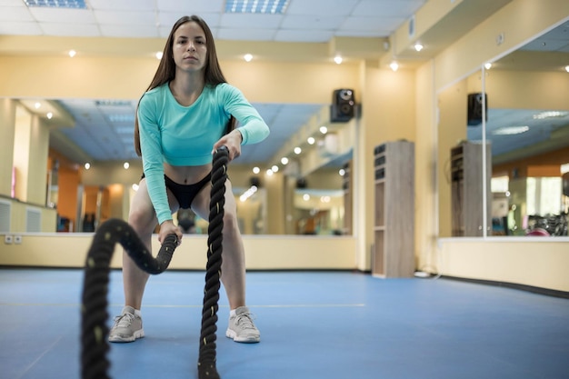 A young woman trains with a battle rope in a fitness room for functional training