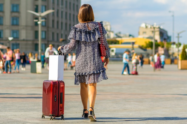 Viaggiatore della giovane donna che porta la sua borsa rossa del carrello sulla via