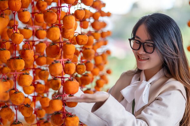 Young woman traveler enjoying dried persimmon hanged on strings to dry a common sight in da lat vietnam by hanging them on a rig and placed in an airtight house good for health