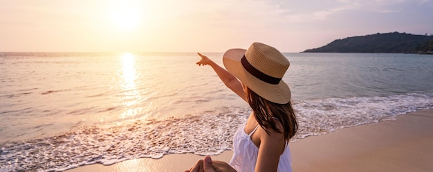 Молодая женщина-путешественница держит мужчину за руку и смотрит на красивый закат на пляже Пара в отпуске летом концепция
