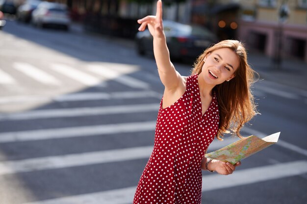 Young woman traveler holding paper map of the city and calling someone on the street in summer