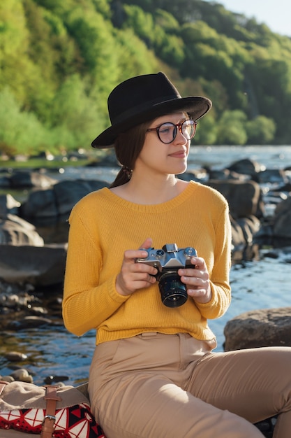 Photo young woman traveler is taking pictures of nature on retro camera