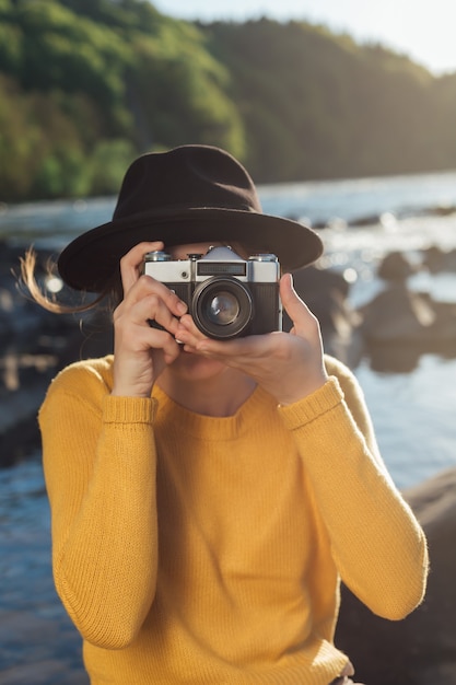 若い女性旅行者はレトロなカメラで自然の写真を撮っています