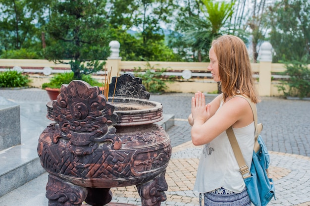 Young woman Traveler praying in polite action with incense sticks at buddhism temple in Vietnam