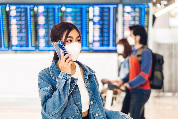 コロナウイルスの検疫中の若い女性旅行者は、国際線ターミナル空港での長期旅行休暇の前に、荷物のように見えるフライト旅行でサージカルマスクの顔の保護を身に着けています