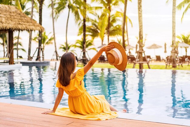 Young woman traveler relaxing and enjoying the sunset by a tropical resort pool while traveling for summer vacation