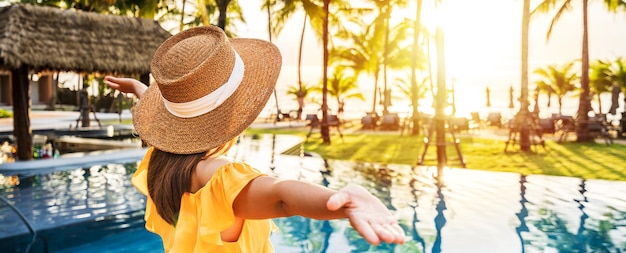 Young woman traveler relaxing and enjoying the sunset by a tropical resort pool while traveling for summer vacation