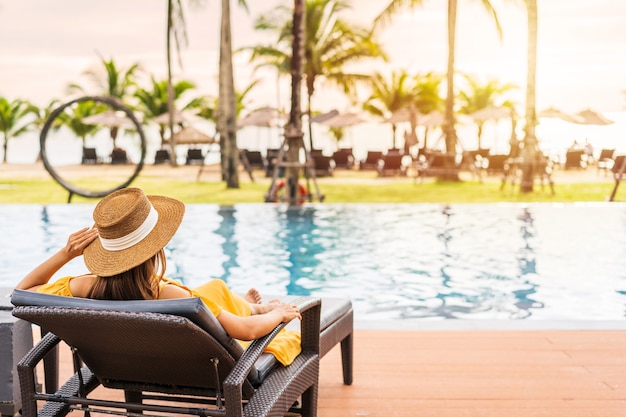 Foto viaggiatore della giovane donna che si rilassa e si gode il tramonto da una piscina tropicale del resort durante il viaggio