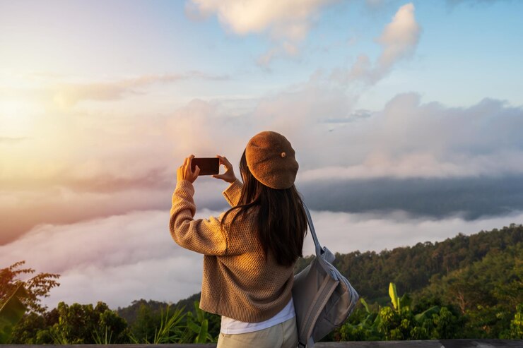 Photo 山の上の霧と日の出の海でスマートフォンで写真を撮る若い女性旅行者
