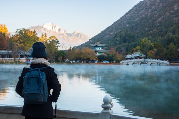 Young woman traveler traveling at Black Dragon Pool with Jade Dragon Snow Mountain , landmark and popular spot for tourists attractions near Lijiang Old Town. Lijiang, Yunnan, China