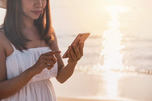 Viaggiatore della giovane donna che per mezzo del telefono cellulare sulla spiaggia tropicale al tramonto, alla vacanza e al concetto di estate