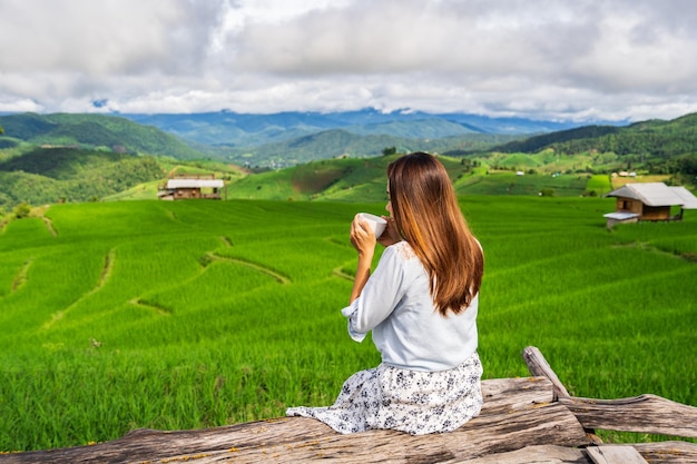 PaPongPiengチェンマイタイの美しい緑の棚田フィールドでコーヒーを飲みながら休暇中の若い女性旅行者