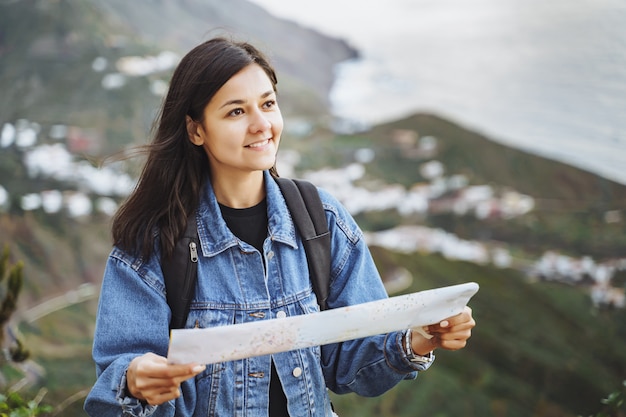 Young woman traveler with a backpack and a map on the background of the ocean and mountains