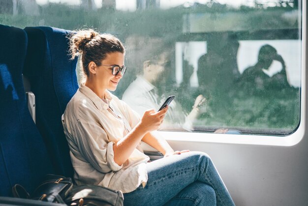 Photo young woman traveling by train and using phone.