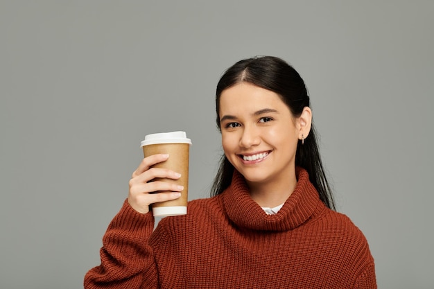 トレンディなセーターを着た若い女性が快適な環境で喜びとスタイルを放射するコーヒーを楽しんでいます